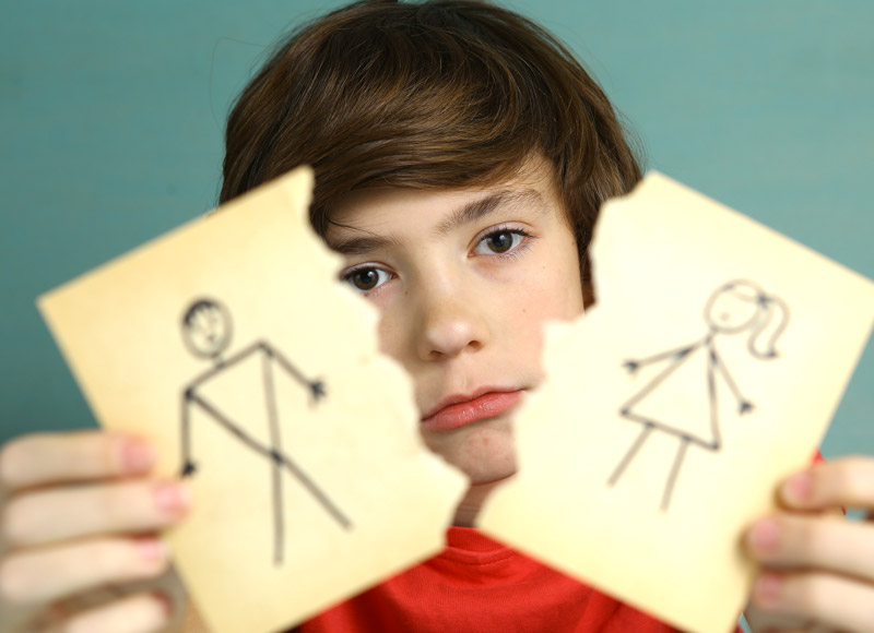 Smutny chłopiec trzymający przedartą na pół żółtą kartkę z rysunkiem rozwodzących się rodziców.